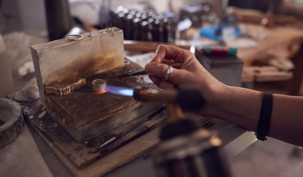Close Up Of Male Jeweller Working On Ring With Blowtorch In Studio
