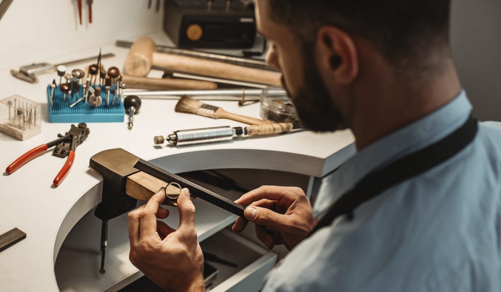  Close up of a male jeweler working and shaping an unfinished ring with a tool