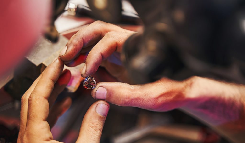 Jeweler is holding cut diamond between fingers
