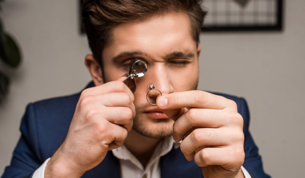 Jewelry appraiser with magnifying glass examining jewelry ring with gemstone in workshop
