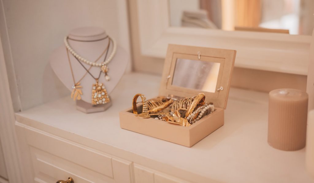 Luxury gold jewelry on set holders and in jewelry box on light dressing table and wardrobe shelves