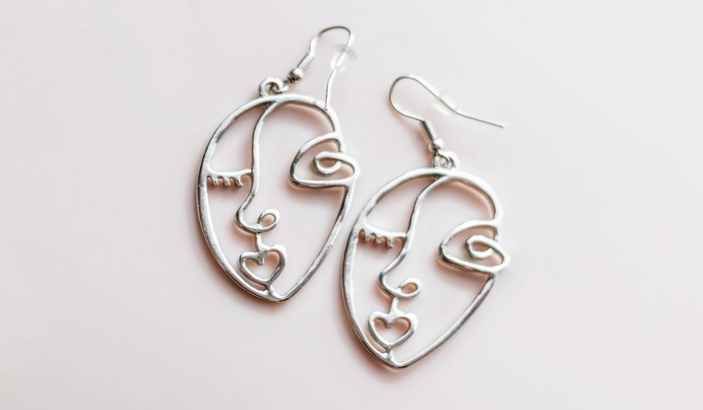 Women's earrings with abstract faces on a pink background.