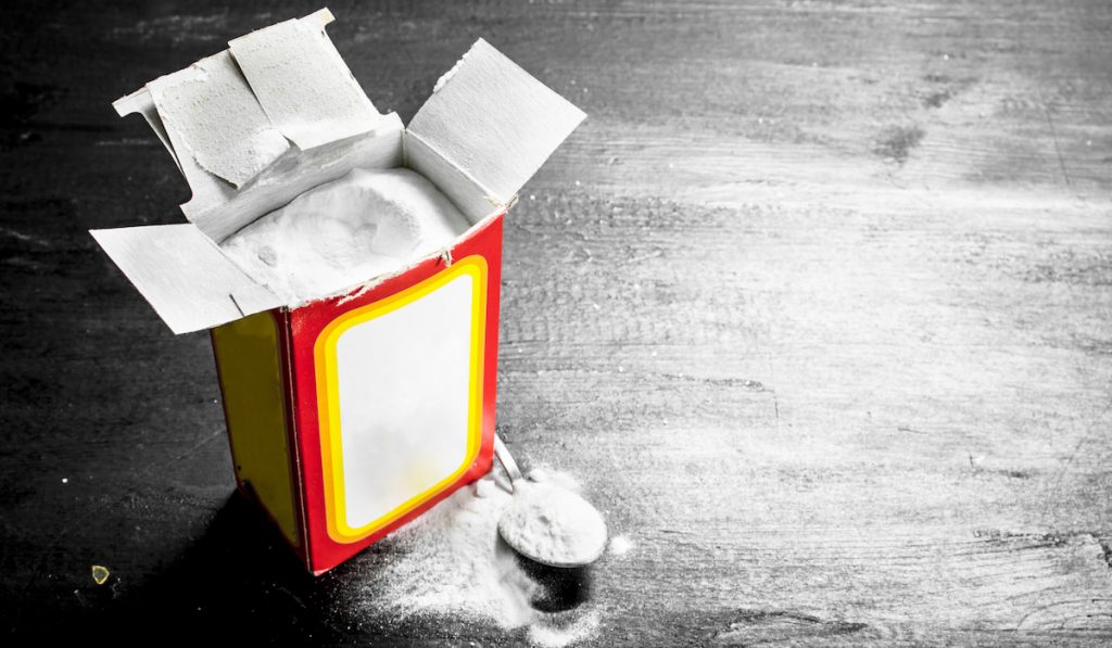 baking soda box and baking soda on a spoon on black table