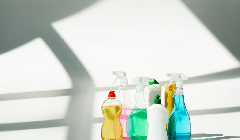 various bottles and sprayers with cleaning products on white background